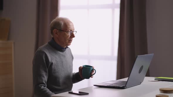 Old Man is Communicating By Video Chat in Laptop with Friends or Family Retiree is Sitting Alone at