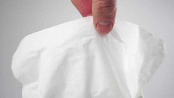 A hand picks up and pulls a white paper facial tissue 