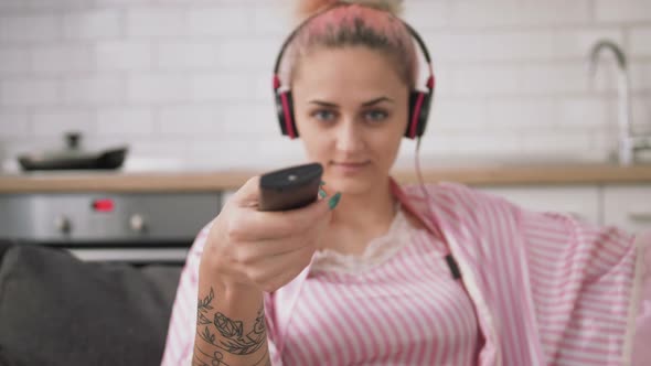 Young Pretty Woman with Pink Hair Watching TV on Sofa in Kitchen Switch Channels Close Up