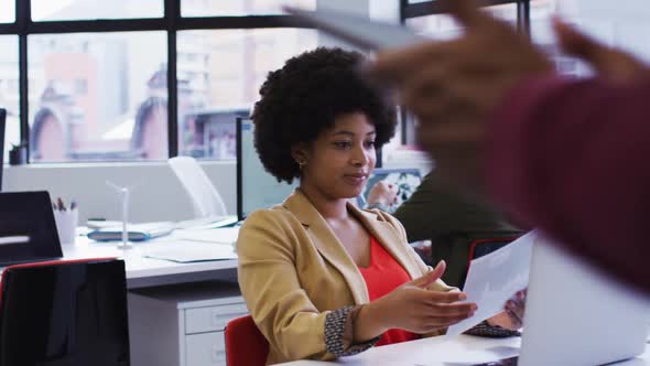 Mixed race businesswoman sitting using a laptop going through paperwork in modern office