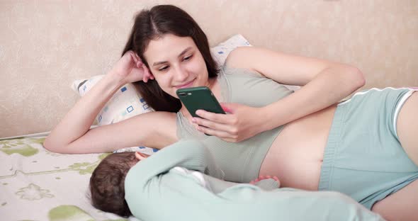 Caucasian Boy Sleeping on the Bed and His Mother Nearby Takes Pictures of Him on a Mobile Phone