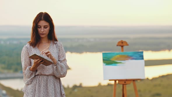 Young Pretty Woman Artist Standing on the Field Holding a Painting Palette  Looking at the Camera