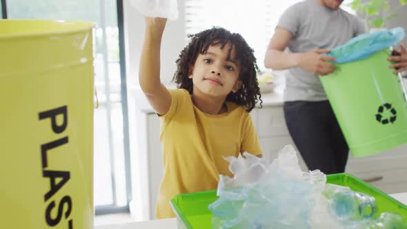 Happy biracial man and his son sorting waste in kitchen