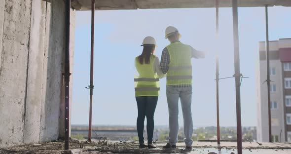 Building Workers Working at Construction Site Builders Looking in Blueprint Back View Copy Space