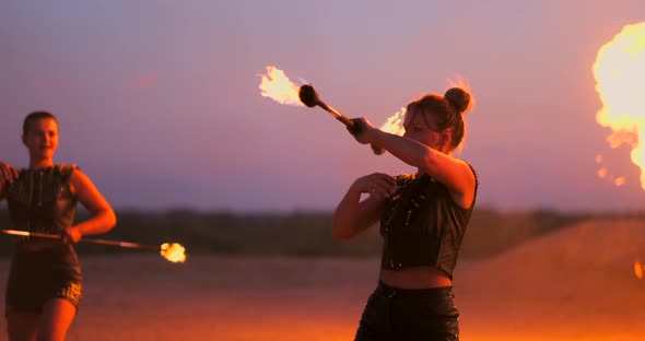 Women with Fire at Sunset on the Sand Dance and Show Tricks Against the Beautiful Sky in Slow Motion