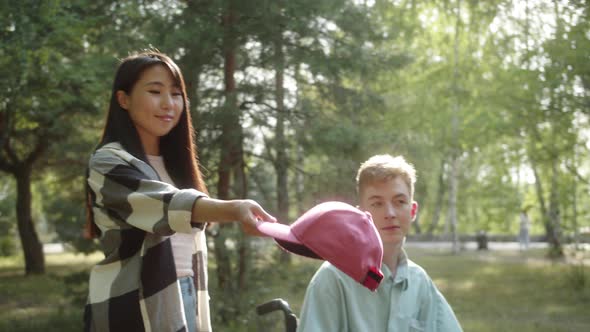 Being in the Public Park with a Disabled Young Blonde Boyfriend a Pretty Asian Girl Gives a Red Cap