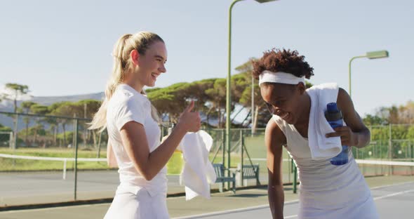 Video of happy diverse female tennis players talking and resting after match