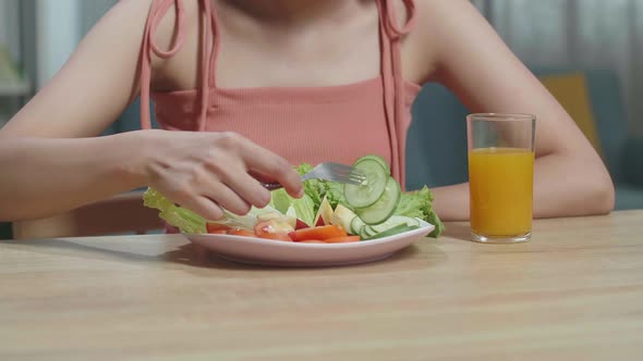 Woman With A Dish Of Healthy Food And A Glass Of Orange Juice Using A Fork Poking Cucumber