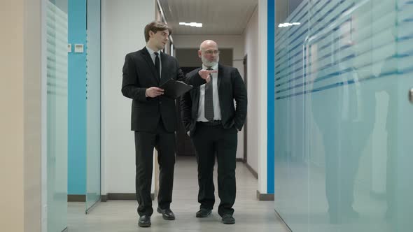 Wide Shot of Young Manager Walking with CEO in Office Corridor Showing Around Talking