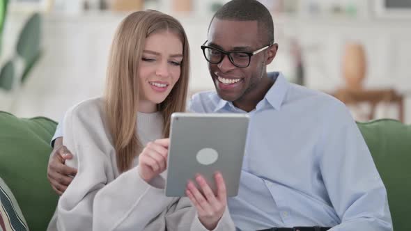 Cheerful Mixed Race Couple Hugging While Using Tablet at Home