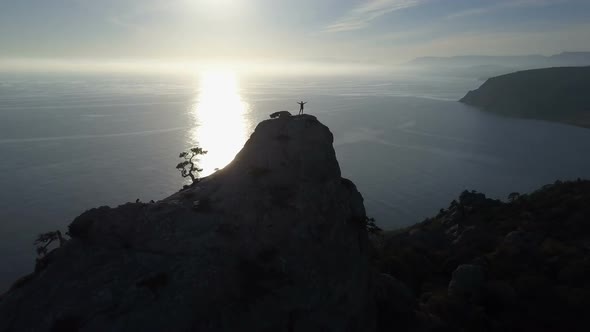 Flight Over of Young Woman Standing on the Top of a Mountain Facing the Sea. Lady on the Summit