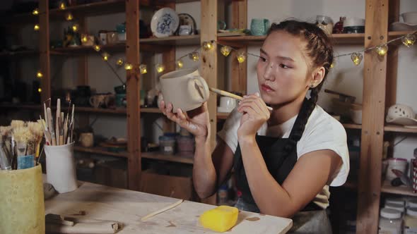 Young Woman Potter Smoothing Out the Clay Cup Using a Wet Brush