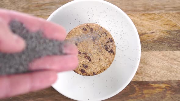 Stacked oatmeal cookies in a white plate on a rustic wooden background. Hand sprinkles poppy seeds