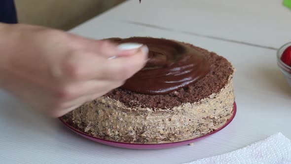 A Woman Applies Chocolate Ganache To A Sponge Cake.