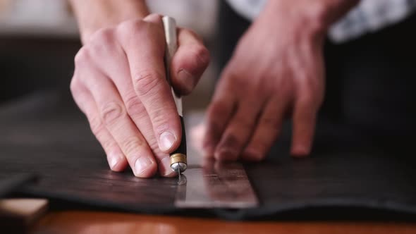 The Tanner Is Cutting Black Leather Sheet with a Razor and Metre