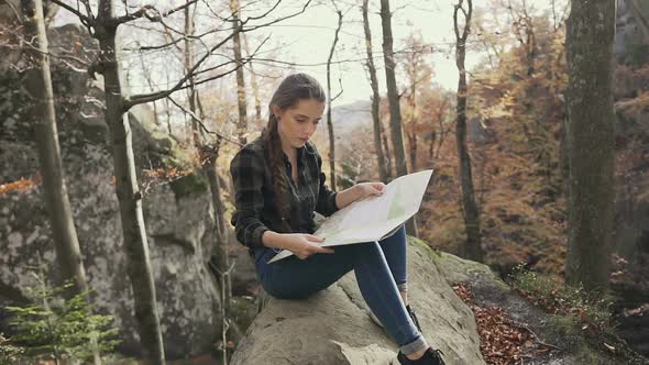 Woman Tourist Sitting on the Cliff in the Woods Looking at Tourist Map