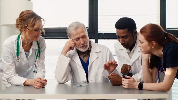 Medical Team of Multiethnic Professional Doctors Looking at Syringe with Coronavirus Vaccine on