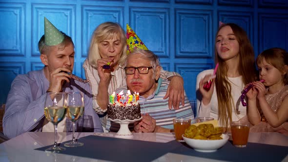 Big Family Celebrating Senior Grandfather Birthday Making a Wish and Blowing on Candles at Home