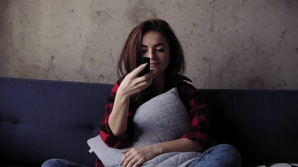 Young Beautiful Brunete Girl is Holding a Pillow While Sitting on Sofa