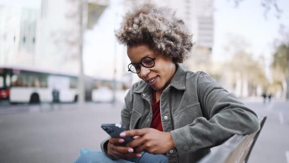 Happy adult African woman wearing casual clothes typing on mobile