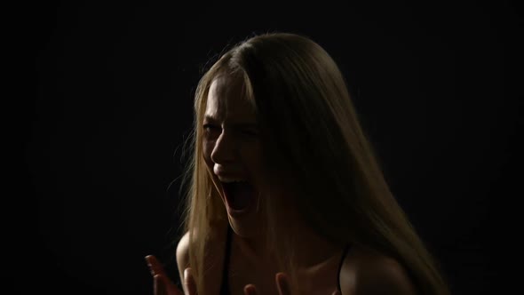 Frightened Woman Screaming and Closing Face With Hands Against Black Background