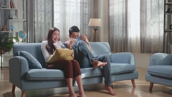 Young Asian Couple Watching Scary Movie On Tv At Home