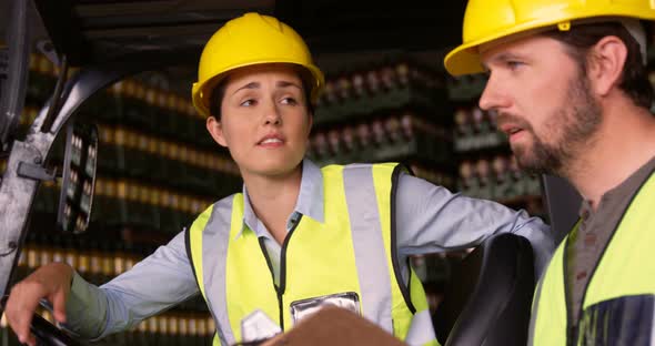 Workers sitting in forklift and talking to each other in warehouse