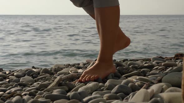 Close-up of a woman's bare feet with their pants rolled up walking on a rocky beach