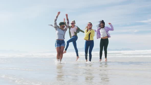 Happy group of diverse female friends having fun, dancing and smiling at the beach