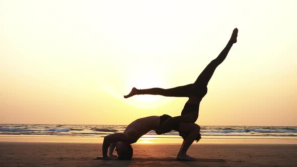 Fit Sporty Couple Practicing Acro Yoga with Partner Together on the Sandy Beach