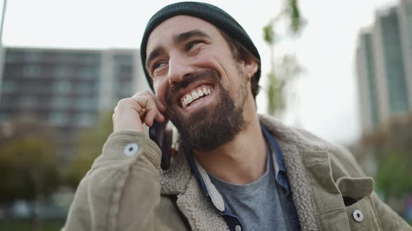 Cheerful bearded man wearing hat talking by phone