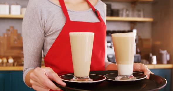 Smiling waitress carrying two cold coffees in cafe