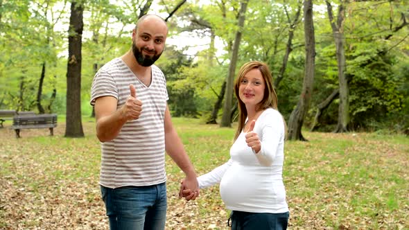 Handsome Man and Young Happy Pregnant Woman Holding Hands and Show Thumbs Up and Smile To Camera