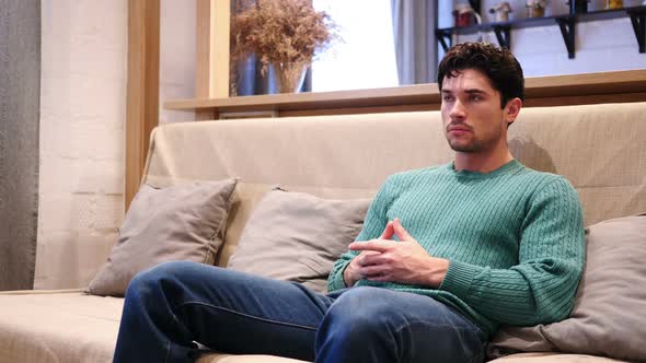 Portrait of Serious Young Man Sitting on Couch at Home