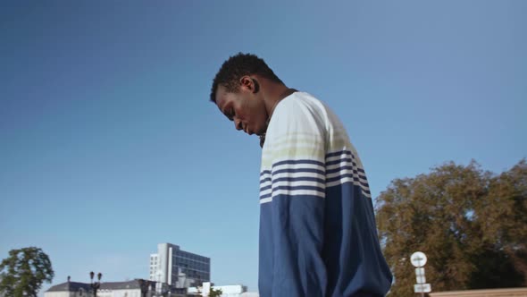 A Young Black Student with Headphones Walks Through the City Centre at Sunset