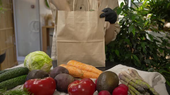 Young Woman Carefully Puts Sorted Vegetables Into Paper Bag