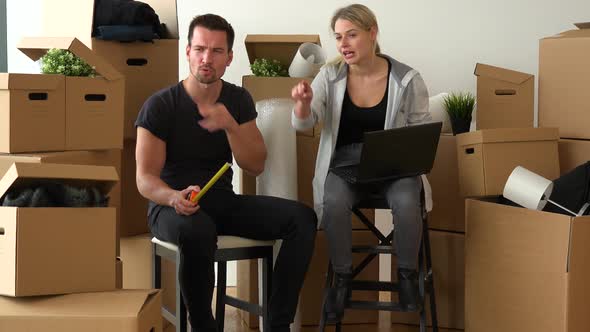 A Serious Moving Couple Sits on Chairs with a Notebook and a Measuring Tape and Discusses Something