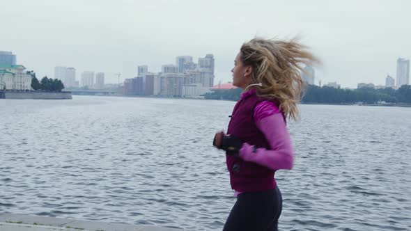 Beautiful Blonde Girl Runs Along Urban Embankment