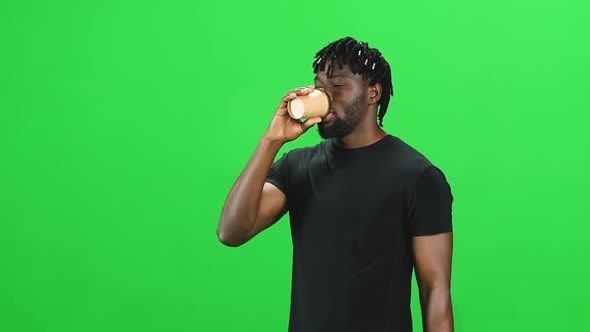 Portrait of African American Man Walking with Dreadlocks and Drinking Coffee at Green Screen. Slow