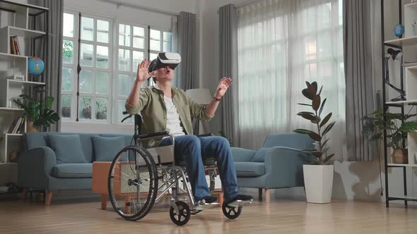 Funny Asian Man Sitting In A Wheelchair While Wearing Virtual Reality Goggles At Home