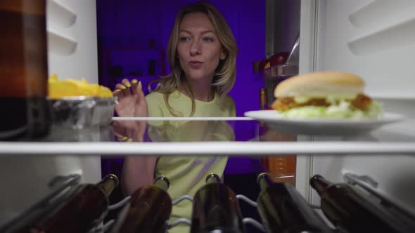 Cheerful Woman Opens the Refrigerator Door at Night Eats Chips and Happy Takes Out Bottle of Beer