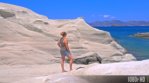 Woman stands on Sarakiniko cliff by turquoise blue Aegean Sea on Milos island, Greece