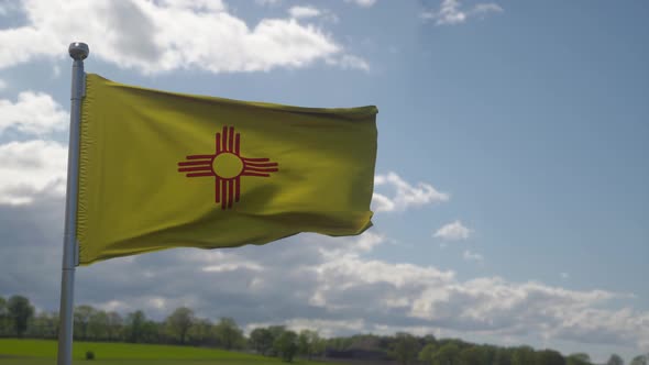 New Mexico Flag on a Flagpole Waving in the Wind Blue Sky Background