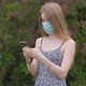 A young girl in a protective medical mask looks at the phone and sends messages - VideoHive Item for Sale