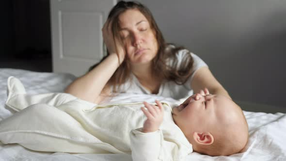 Tired Mother Sleeps Sitting on Floor Near Crying Baby Girl