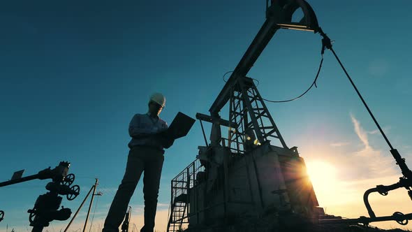 Oil Industry Worker Walking in Front of an Oil Derrick in Sunlight. Slow Motion