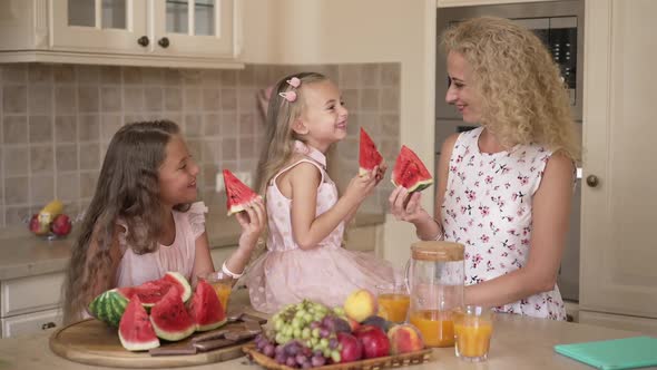 Happy Laughing Mother and Daughters Eating Delicious Watermelon in Kitchen at Home