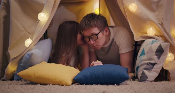 Cute Little Daughter and Handsome Young Dad Sharing Secrets Smiling While Playing Together in Teepee