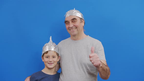 Grandfather with His Grandson in Protective Foil Hats From 5g Radiation Standing on a Blue