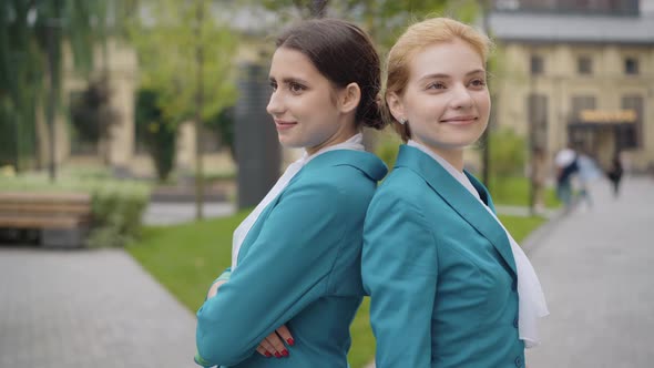 Elegant Young Caucasian Women in Stewardess Uniform Standing Back To Back with Crossed Hands and